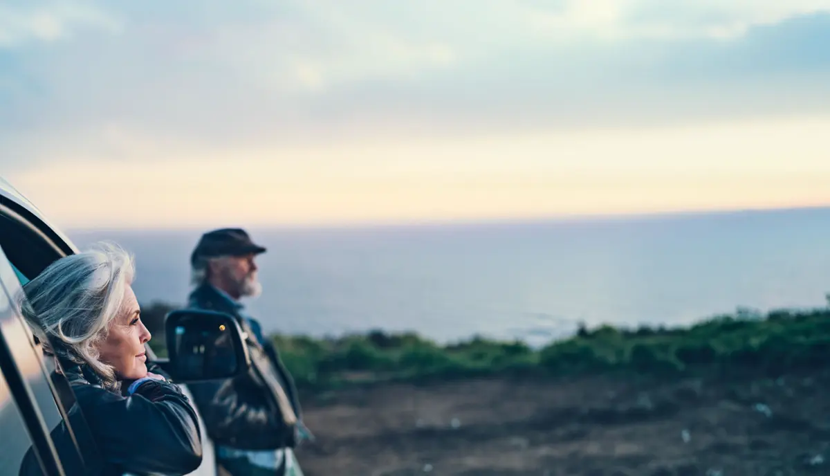 Pareja de adultos mayores mirando el horizonte del mar al atardecer