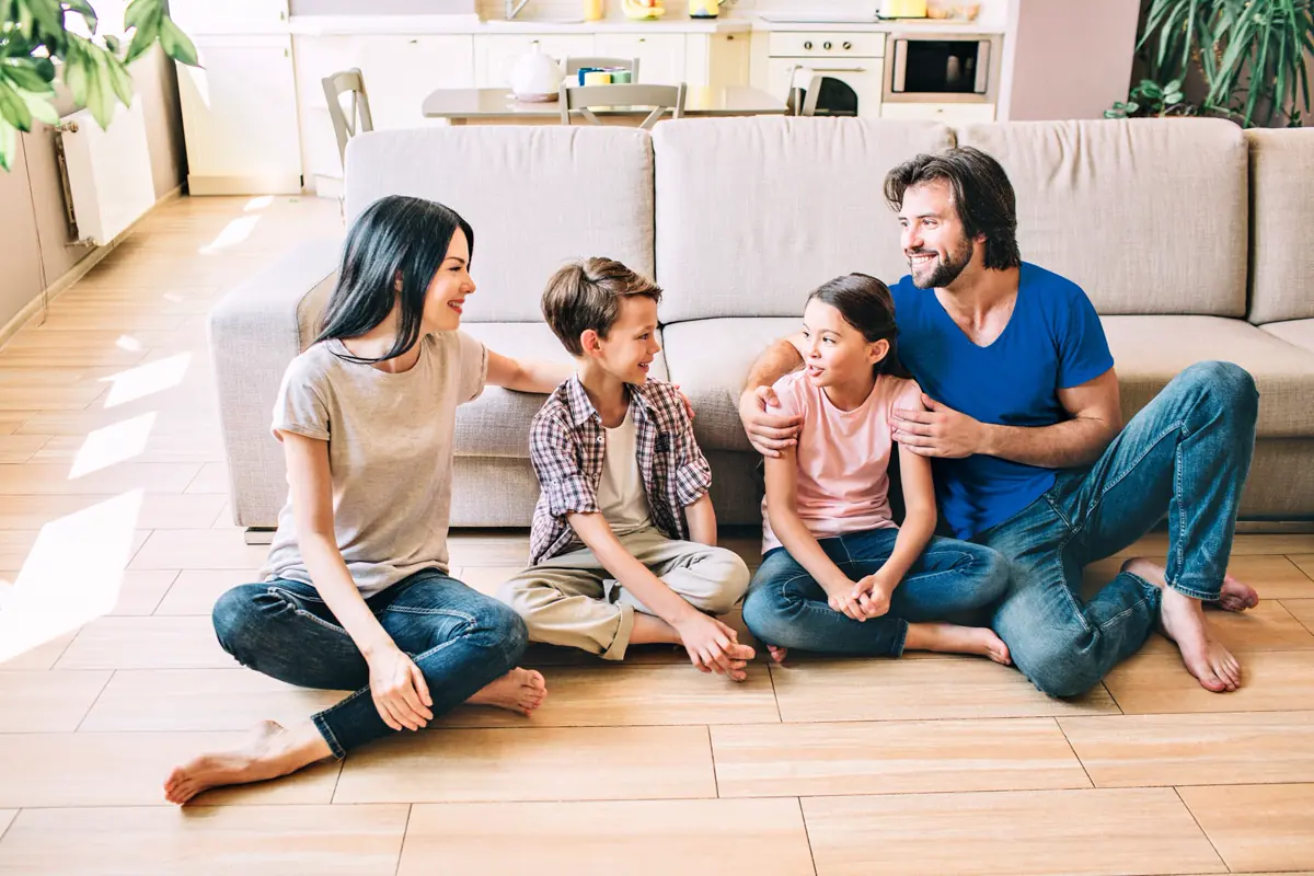 Familia con dos hijos sentada en el piso de una sala, conversando y sonriendo