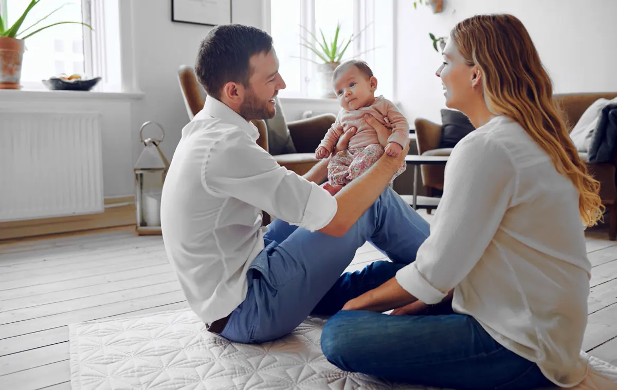 Pareja joven jugando en el piso con su bebé en un hogar luminoso